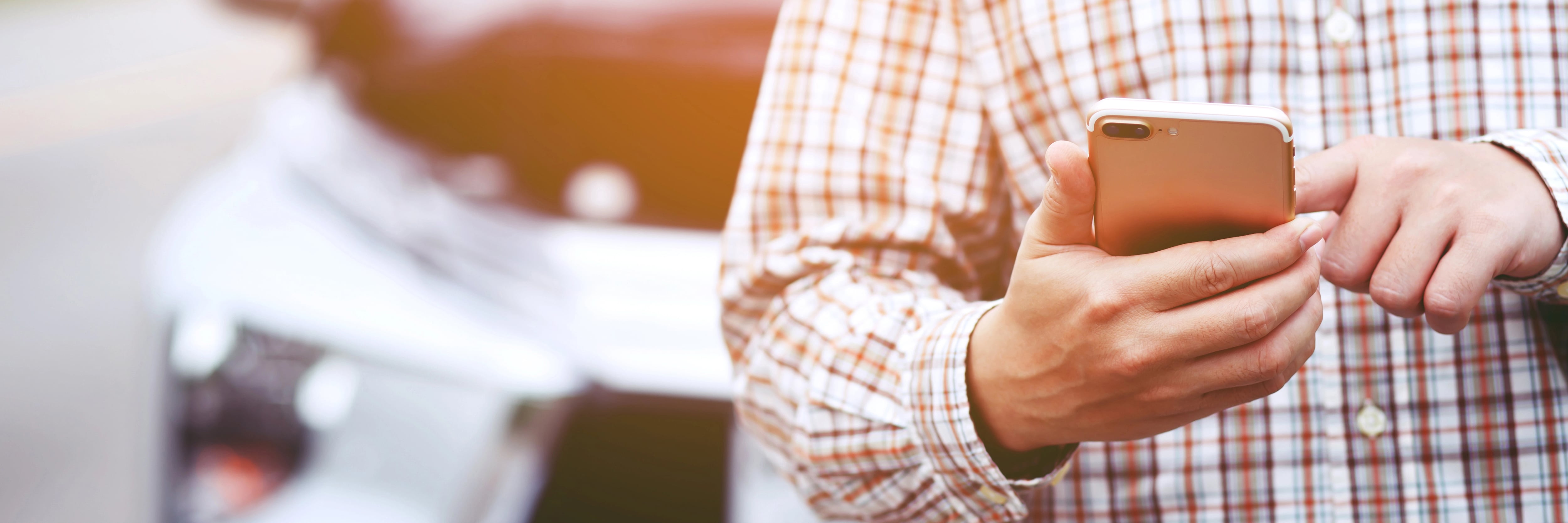 Man holds a mobile phone with a car in the background